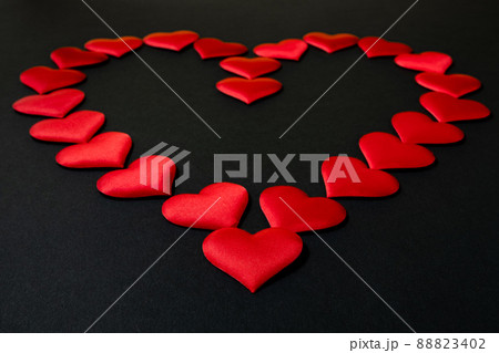A large red heart, laid out of many small identical red silk hearts, on a black background. A symbol of love and passion 88823402
