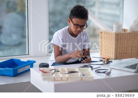 A dark-skinned boy constructing a transformer and looking busy 88829669