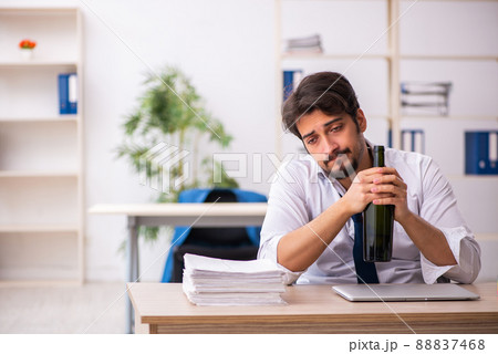 Young alcohol addicted employee sitting in the office Young alcohol addicted employee sitting in the office 88837468