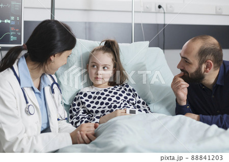 Happy smiling father being attentive to pediatrist expert talking about successful recovery of daughter. Healthcare pediatric clinic medic doing checkup to ill girl while in recovery ward room. Happy smiling father being attentive to pediatrist expert talking about successful recovery of daughter. Healthcare pediatric clinic medic doing checkup to ill girl while in recovery ward room. 88841203