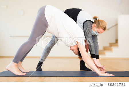 Pregnant woman practices yoga with an instructor wearing an antiviral mask during quarantine. Downward Dog Pose or Adho Mukha Svanasana 88841721