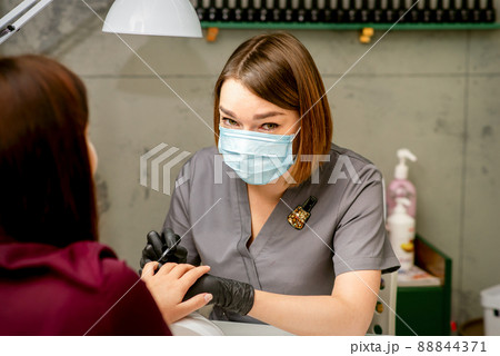 Portrait of young caucasian manicure master wearing protective mask painting female nails in a beauty salon 88844371