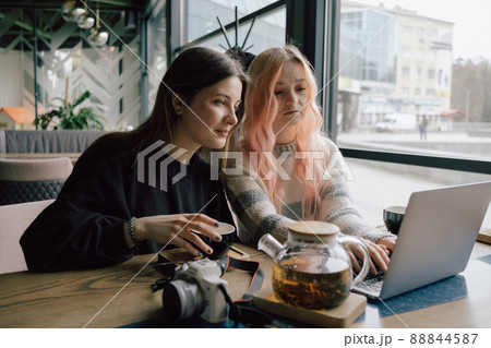 two happy young women sitting in coffee shop looking at laptop computer 88844587