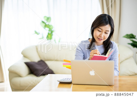 在宅ワークでメモをとりながらパソコン画面を見る30代女性 88845047