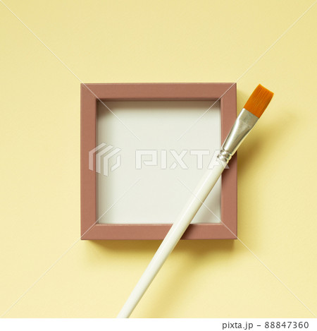 Pink picture frame with paint brush on yellow background. top view, copy space 88847360