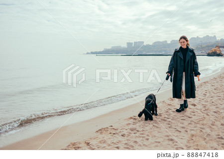 Young woman in a black coat walking her dog Young woman in a black coat walking her dog 88847418