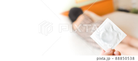 Human hand holding a packed condom against a blurred female background in white bed,copy space Human hand holding a packed condom against a blurred female background in white bed,copy space 88850538
