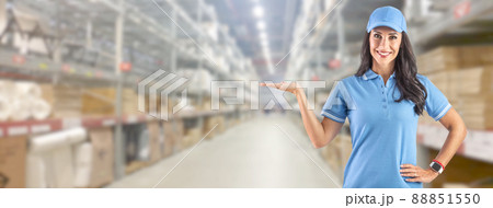 Young delivery woman in work clothes in front of a huge warehouse her left hand offers free space for information Young delivery woman in work clothes in front of a huge warehouse her left hand offers free space for information 88851550