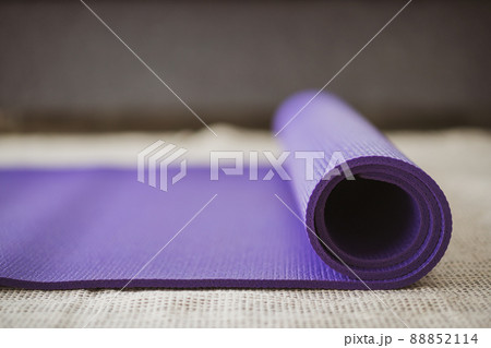 Rolled purple yoga exercise mat on the floor in living room close up with copyspace. Indoor workout activity concept. Rolling Purple Yoga carpet close up. 88852114