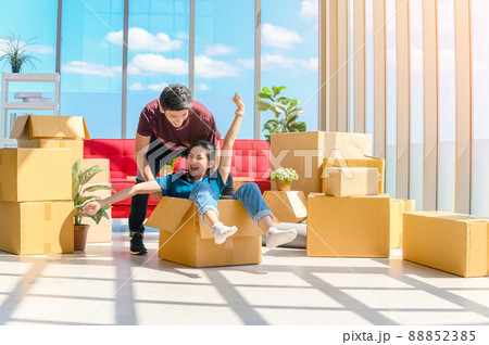 Happy young asian couple smiling relaxing and having fun while playing with cardboard box in new house, celebrating moving to new home concept Happy young asian couple smiling relaxing and having fun while playing with cardboard box in new house, celebrating moving to new home concept 88852385