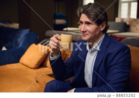 Customer, handsome man in business suit enjoying coffee break sitting on the sofa in a furniture store, waiting for a consultation of an interior designer about the new project of home remodelling 88855202