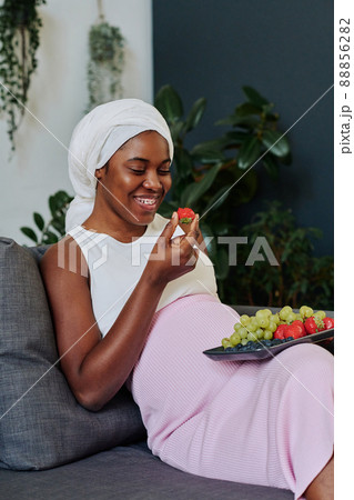 African muslim woman in hijab sitting on sofa and eating fresh fruits during her pregnancy 88856282