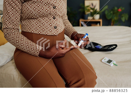 Close-up of pregnant woman using glucometer to control her blood sugar level in finger while sitting in bedroom 88856325