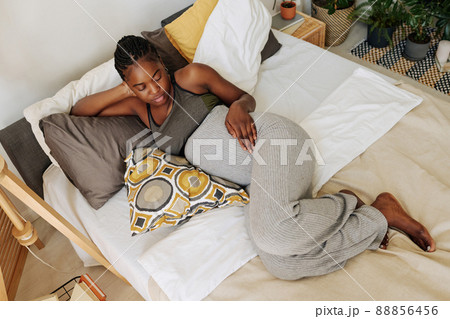 High angle view of African young girl looking at her pregnant belly while relaxing on cushions in bed 88856456