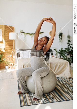 African pregnant girl doing stretching exercises on fitness ball in morning in her bedroom African pregnant girl doing stretching exercises on fitness ball in morning in her bedroom 88856477
