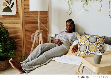 Portrait of African girl touching her pregnant belly while lying on her bed and resting in bedroom 88856499