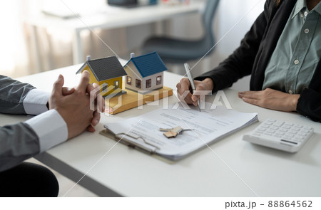 Real estate agent assisting client to sign contract at desk with house model 88864562