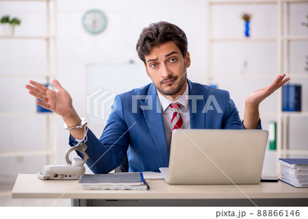 Handcuffed young male employee sitting in the office Handcuffed young male employee sitting in the office 88866146