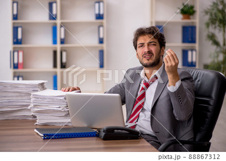 Young male employee unhappy with excessive work in the office Young male employee unhappy with excessive work in the office 88867312