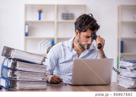 Young male employee unhappy with excessive work in the office Young male employee unhappy with excessive work in the office 88867882