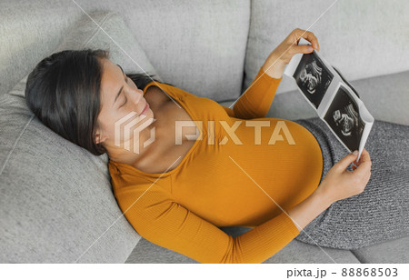 Baby ultrasound scan. Pregnant Asian woman holding hospital picture result from health checkup with small belly happy of first pregnancy 88868503