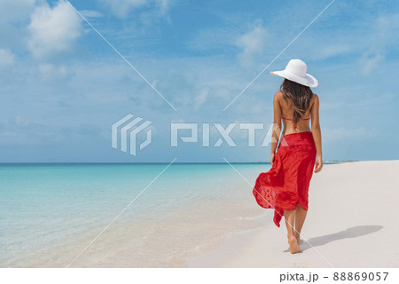 Luxury beach vacation elegant tourist woman walking relaxing in red beachwear and sunhat on white sand Caribbean beach. Lady tourist on holiday vacation resort 88869057
