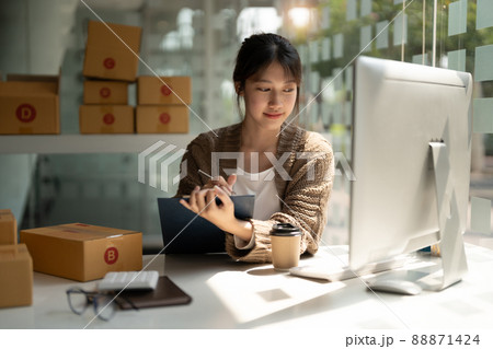 Young woman small business owner online shopping at home. list orders from customers with mobile phones preparing package product on background. SME entrepreneur or freelance life style concept. 88871424