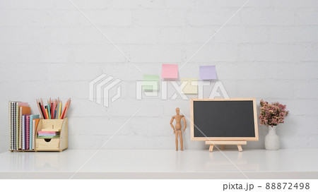 Chalkboard, potted plant and stationery on white table against brick wall. Copy space for your information content. 88872498