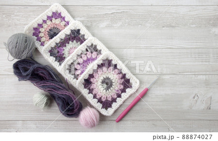 Granny squares crochet in pink and purple shades , a hook and yarn balls. 88874027