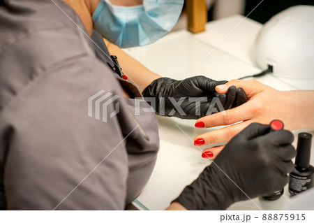 Professional manicure. A manicurist is painting the female nails of a client with red nail polish in a beauty salon, close up. Beauty industry concept Professional manicure. A manicurist is painting the female nails of a client with red nail polish in a beauty salon, close up. Beauty industry concept 88875915