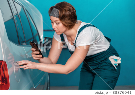 Female mechanic in overall check with device scratches of car. The concept of women's equality and automobile service Female mechanic in overall check with device scratches of car. The concept of women's equality and automobile service 88876041