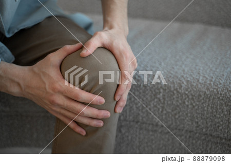 Man massages knee feeling acute joint pain sitting on sofa Man massages knee feeling acute joint pain sitting on sofa 88879098
