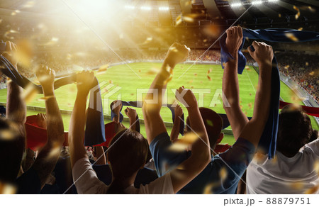 Rear view of football, soccer fans cheering their team with scarfs at crowded stadium at evening time. Concept of sport, support, competition. Out of focus effect 88879751