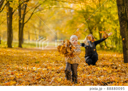 Little daughter and mother have fun in the park among the fallen yellow leaves on a sunny autumn day. 88880095