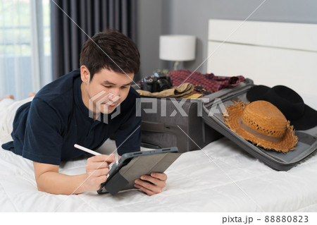 man writing tablet and packing clothes into suitcase on a bed at home, planning travel holiday. man writing tablet and packing clothes into suitcase on a bed at home, planning travel holiday. 88880823