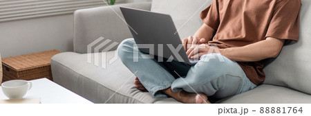 Technology Concept The male who is wearing casual clothes sitting on the sofa, resting his notebook on his lap and doing his work 88881764