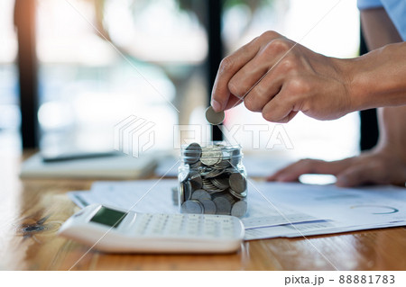 Saving concept the man dropping a coin into the glass bottle with full coins 88881783