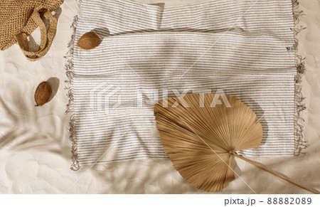 Striped linen beach towel with fringes and two coconuts on sandy beach with shadows from palm tree. Relaxation and tropical summer holidays concept Striped linen beach towel with fringes and two coconuts on sandy beach with shadows from palm tree. Relaxation and tropical summer holidays concept 88882089