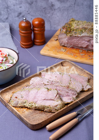 Roasted turkey thigh on a wooden board, cut into pieces. In the background is a bowl of vegetable salad and a turkey. Close-up. 88885446