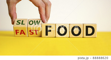 Male hand flips a wooden cube and changes the inscription 'fast food' to 'slow food'. Beautiful yellow table, white background. Healthy and unhealthy lifestyle concept. Male hand flips a wooden cube and changes the inscription 'fast food' to 'slow food'. Beautiful yellow table, white background. Healthy and unhealthy lifestyle concept. 88888620