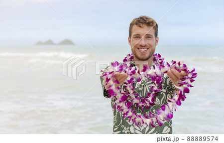 Hawaii welcome caucasian man in hawaiian shirt welcoming tourist giving lei of fresh flowers as aloha spirit gesture on Hawaii beach for luau party. Travel vacation destination 88889574