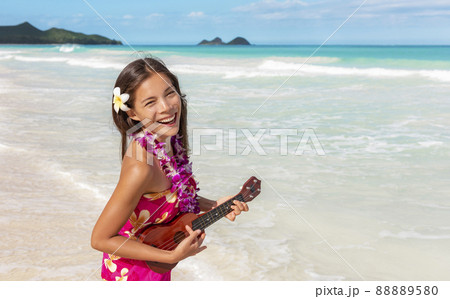 Hawaii luau ukulele hula dancing woman playing guitar on beach vacation with flower lei necklace and paero. Asian dancer smiling on hawaiian travel vacation 88889580
