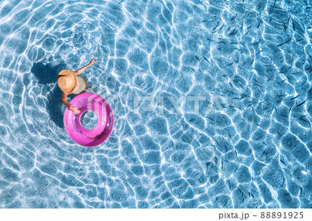 Aerial view of a young woman in hat swimming with pink swim ring in blue sea with school of fish Aerial view of a young woman in hat swimming with pink swim ring in blue sea with school of fish 88891925