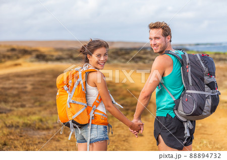 Happy young couple tourists in love holding hands walking on trek hike with backpacks. Hikers on nature travel hiker trail destination smiling happy. Interracial relationship 88894732