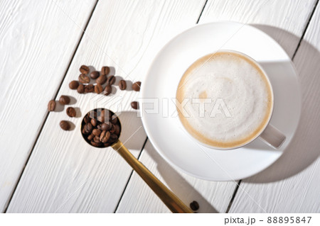 cup of cappuccino coffee on white wooden table and coffee beans, having a break, time for relax and digital detox top view. cup of cappuccino coffee on white wooden table and coffee beans, having a break, time for relax and digital detox top view. 88895847