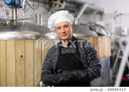 Successful brewer standing in brewery near fermentation tanks Successful brewer standing in brewery near fermentation tanks 88896419