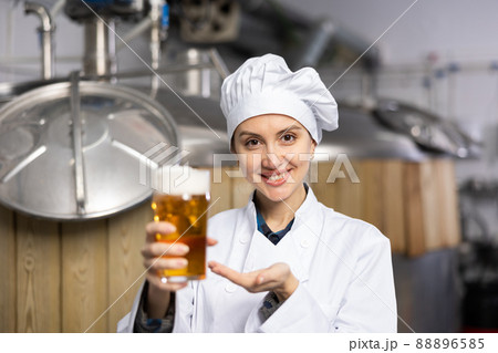 Positive woman brewer presenting glass of fresh beer Positive woman brewer presenting glass of fresh beer 88896585