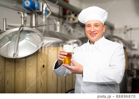 Satisfied professional brewer holding out glass with craft beer Satisfied professional brewer holding out glass with craft beer 88896870