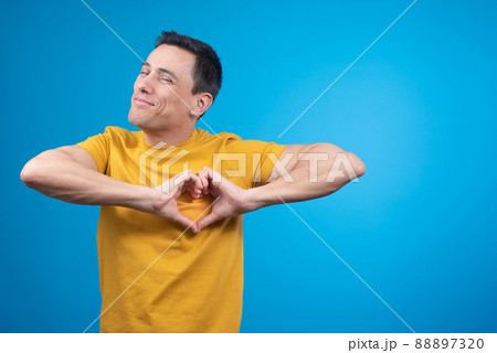 Smiling man gesturing heart on chest in blue studio 88897320