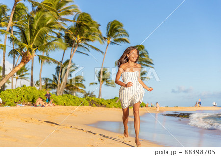 Summer vacation happy Asian woman running carefree on beach during Hawaii travel on Maui island wearing white dress at sunset 88898705